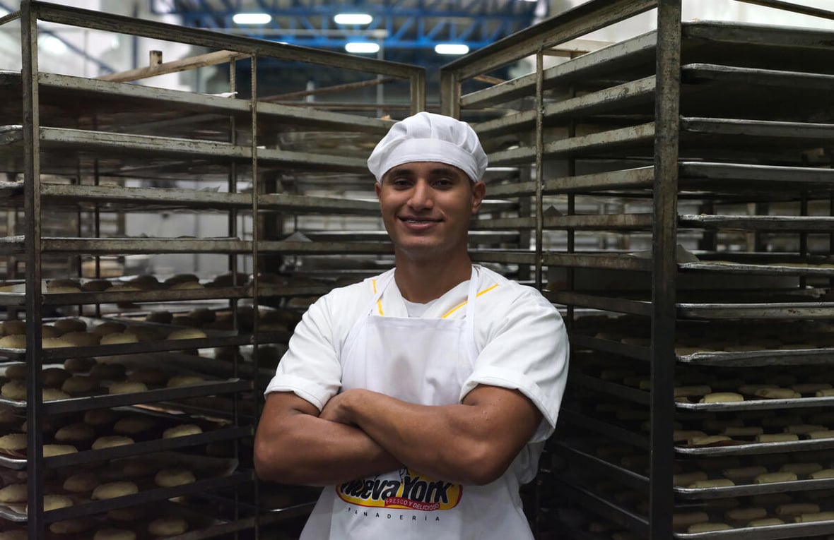 A man stands smiling in front of rows of unbaked bread