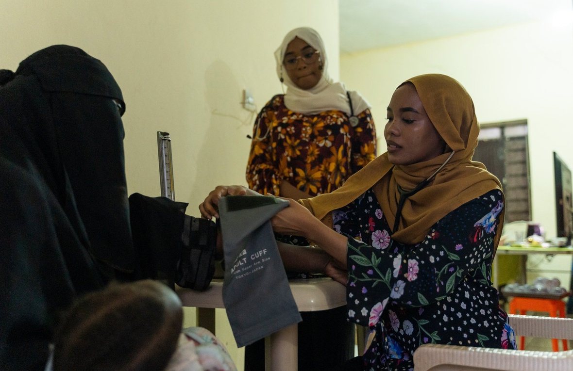 A young woman takes another woman's blood pressure while a third woman looks on.