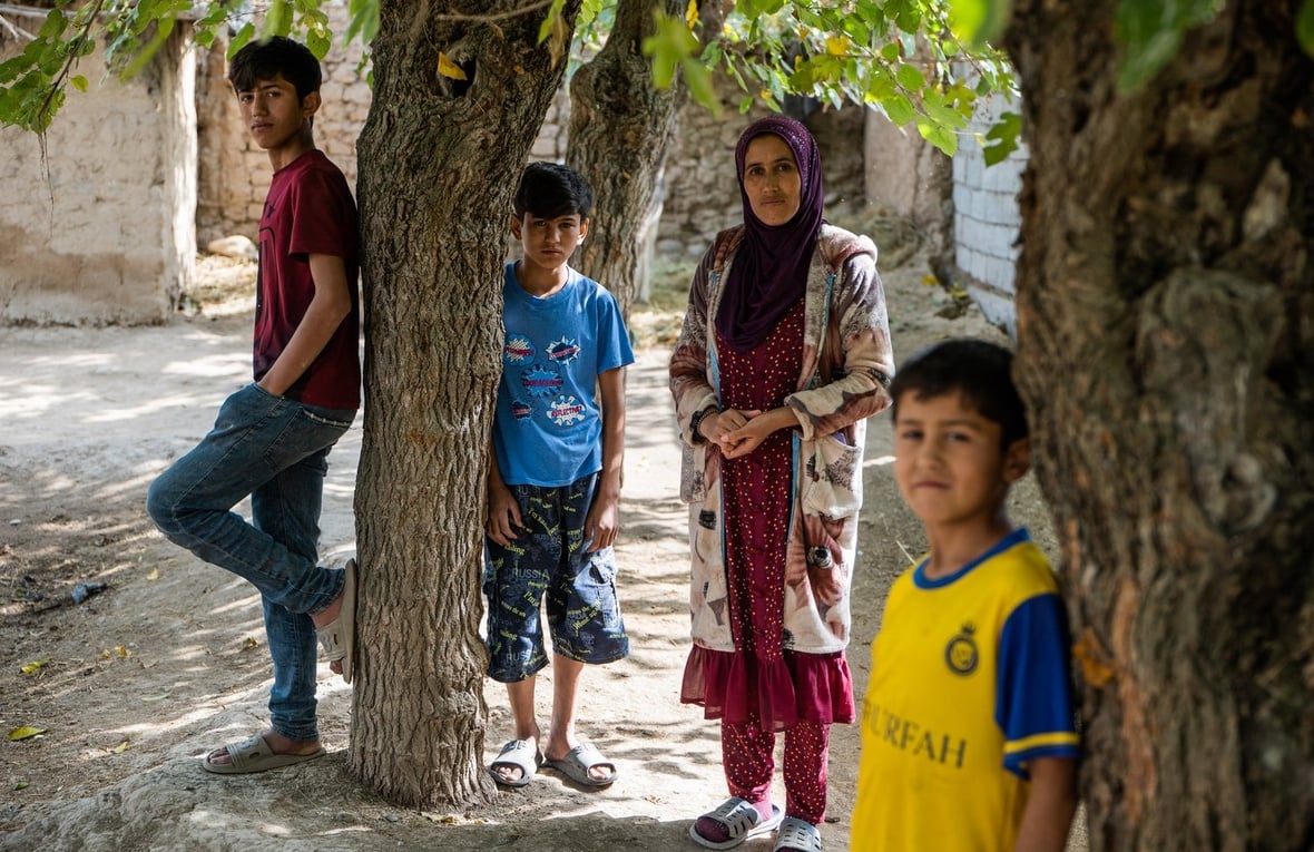 A woman stands amongst some trees with three boys of different ages.