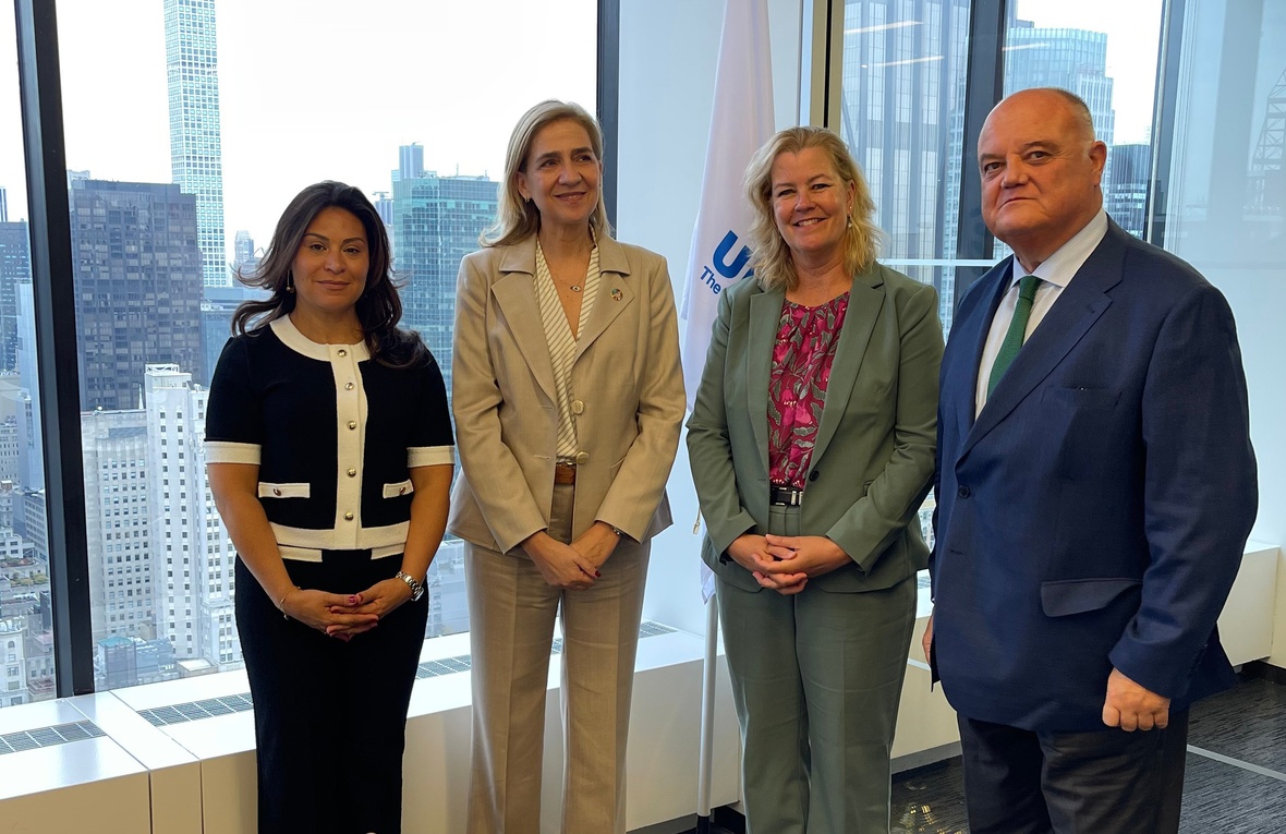 Four people stand looking at the camera inside an office building, a view of New York city behind them through the window.