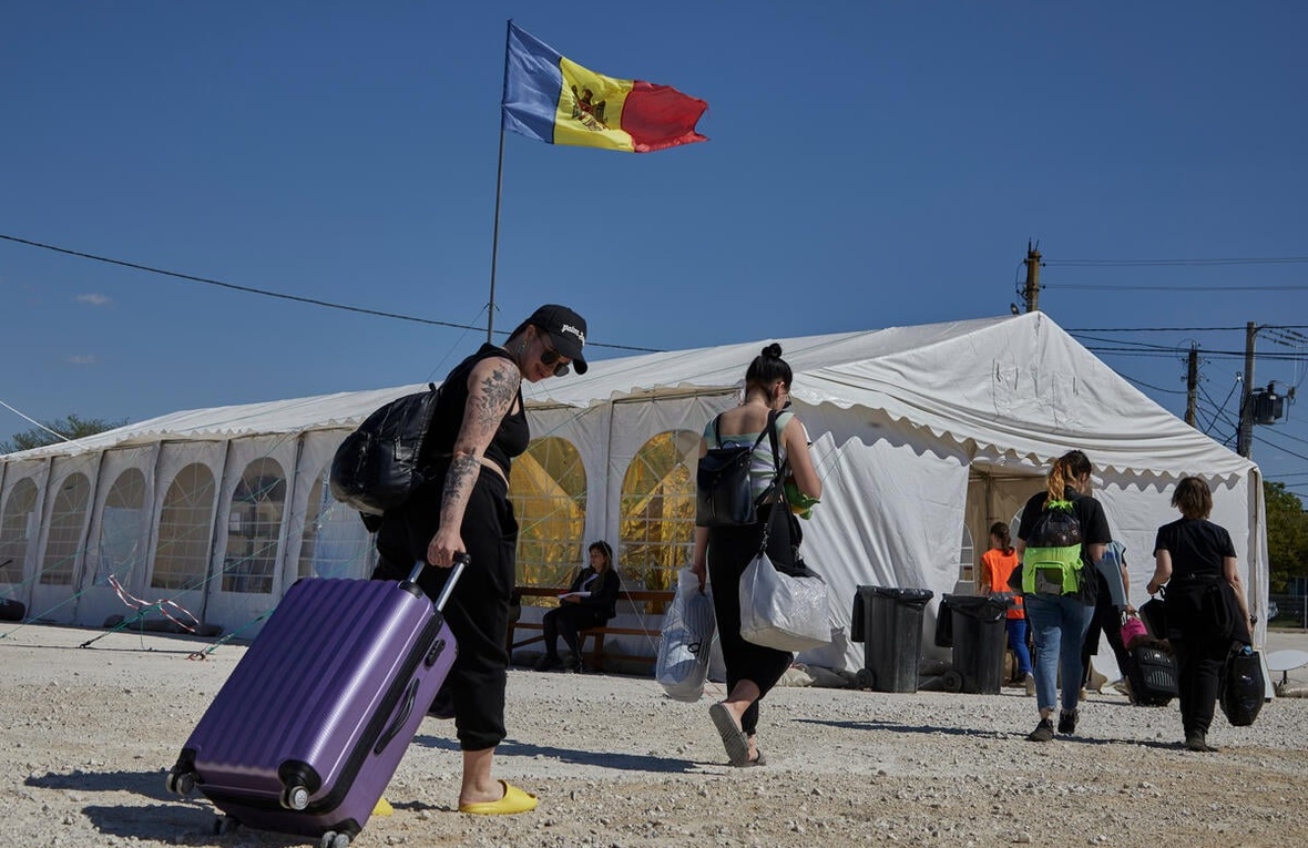 People carrying bags and pulling suitcases walk towards a large tent with a Moldovan flag flying above it
