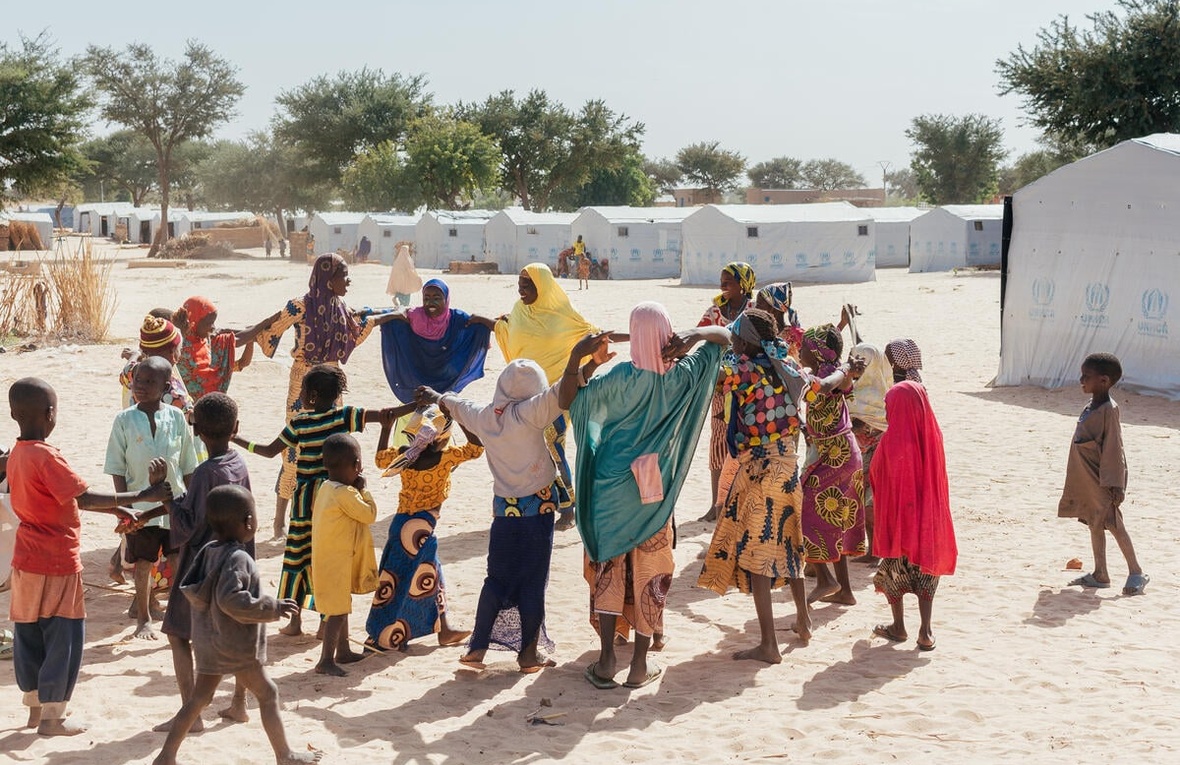 A group of Nigerian refugees play outside, with UNHCR tents in the background.