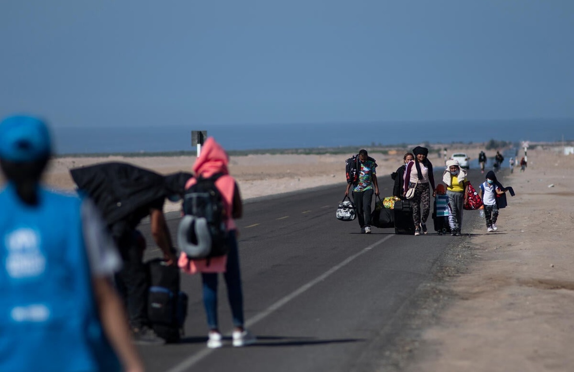 Refugees walk on a highway, with the sea in the background