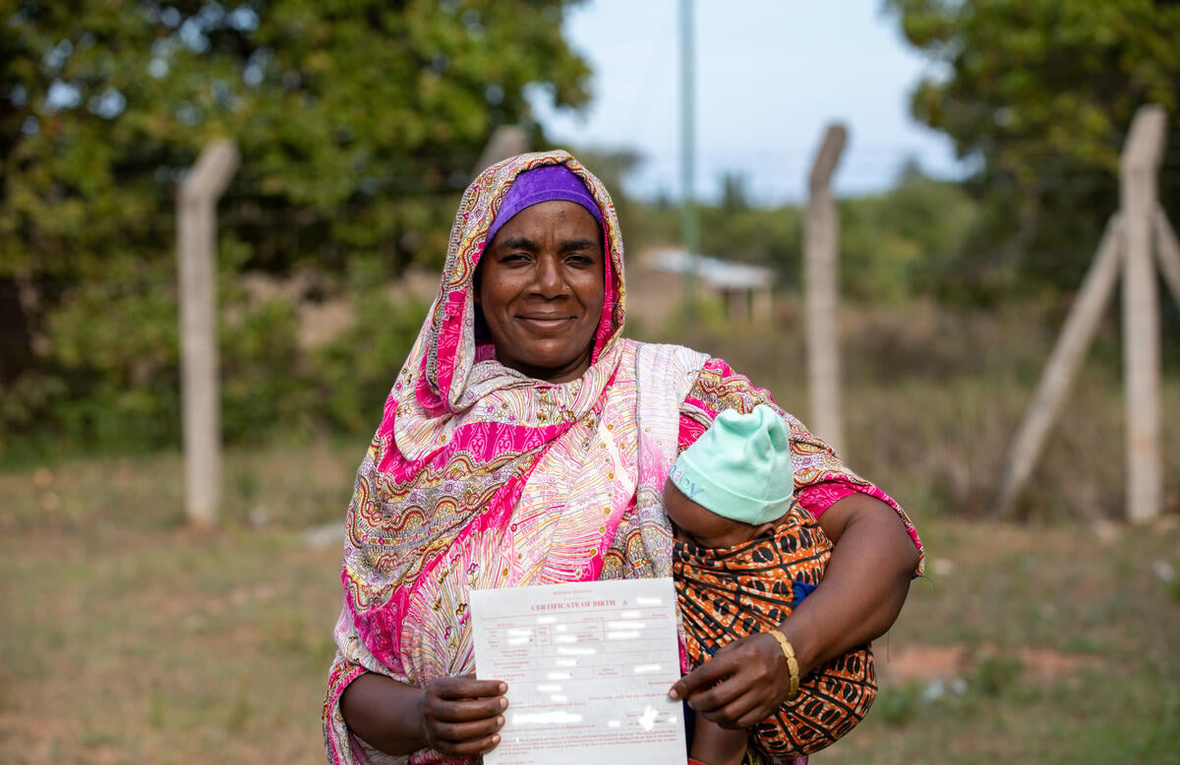 A Pemba woman from Kenya smiles while holding a baby in her arms, proudly displaying a document.