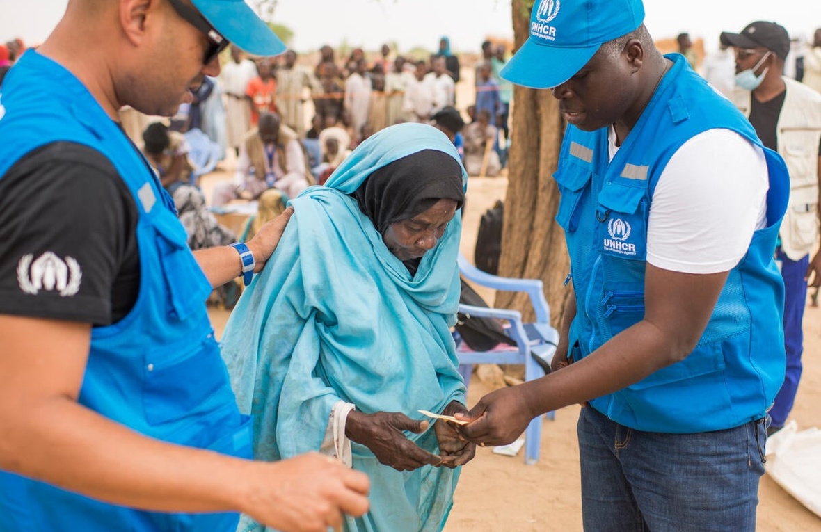 Two UNHCR staff members speak with an elderly Sudanese refugee woman. 
