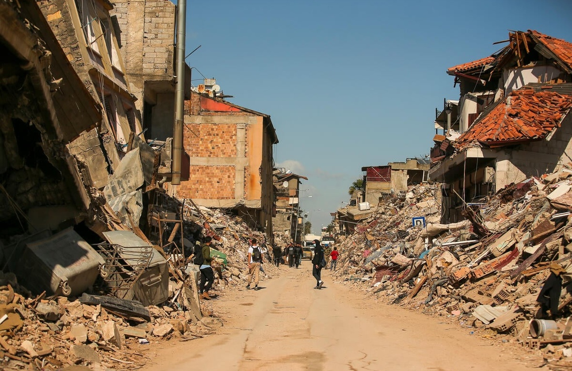 Residents walk past the rubble of destroyed buildings shortly after the earthquakes in Hatay, Türkiye.