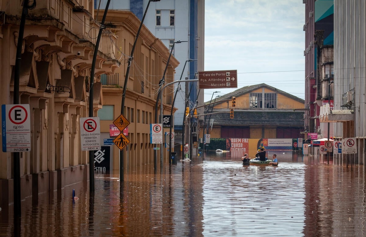 Several people standing in floodwaters in a historic street, with some people in a small boat.