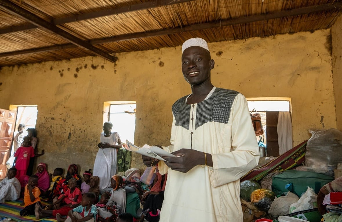 A young man holds some documents in a crowded room.