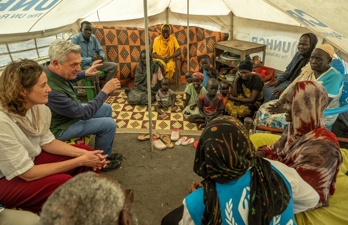UN High Commissioner for Refugees Filippo Grandi seated in a circle with a large refugee family inside a UNHCR tent.