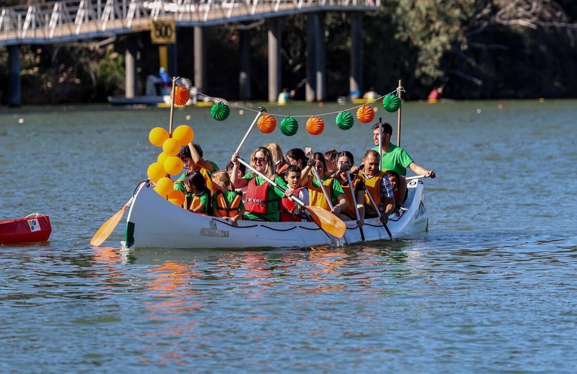 Men, women and children paddle a canoe decorated with green and orange paper lanterns and balloons.