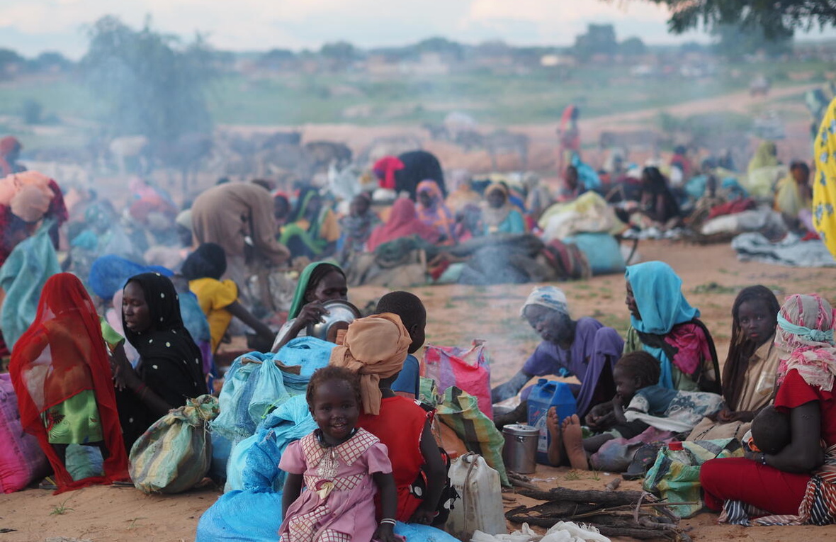 Women and children sit on the ground with their belongings.