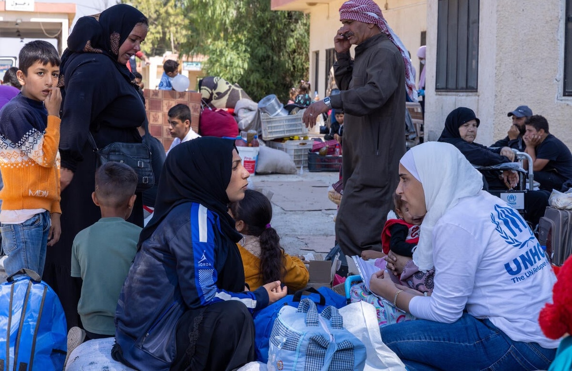 Syrian and Lebanese people sit on the ground in groups at a border crossing.