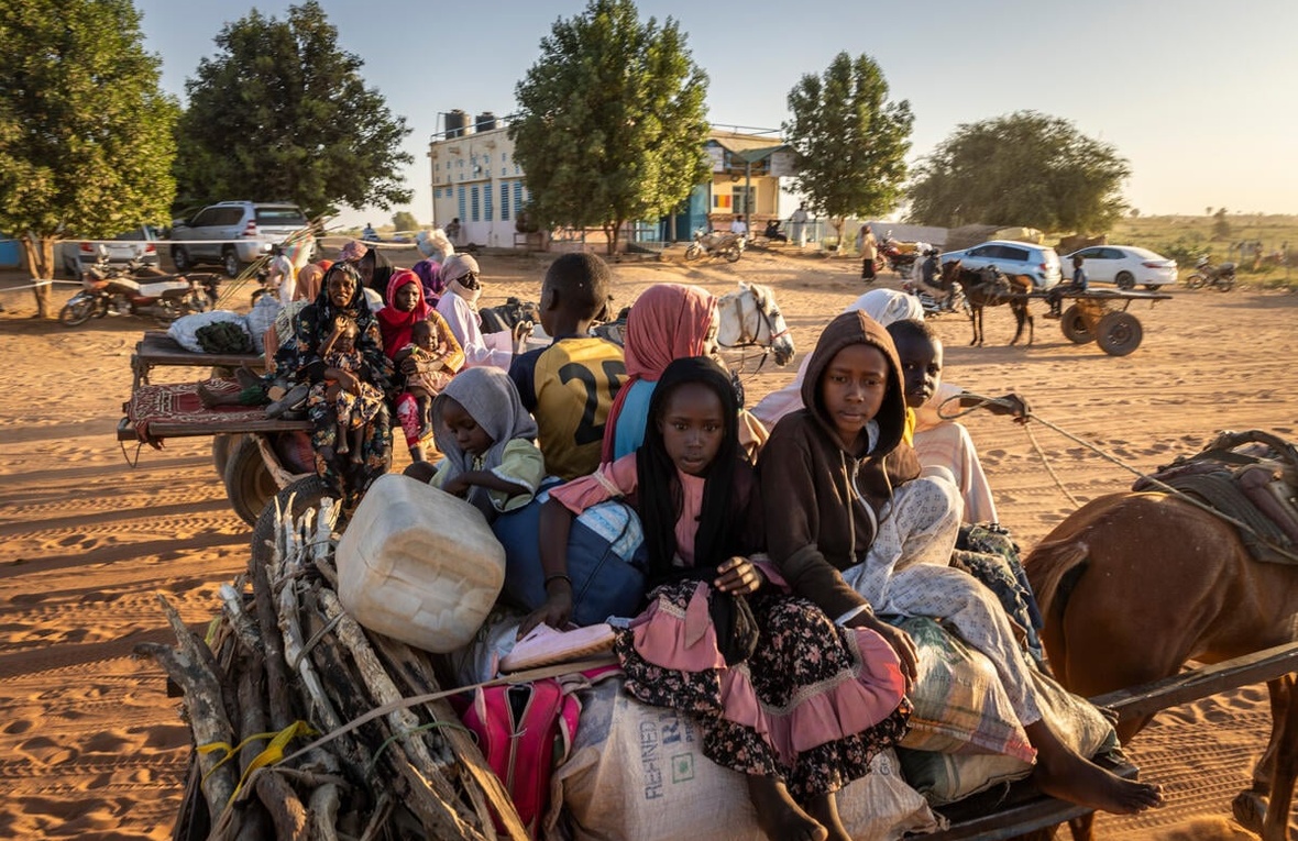 Sudanese refugees are transported on carts behind horses across a dry environment