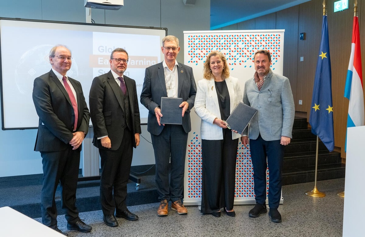 Four men and one woman stand looking at the camera while holding up two documents