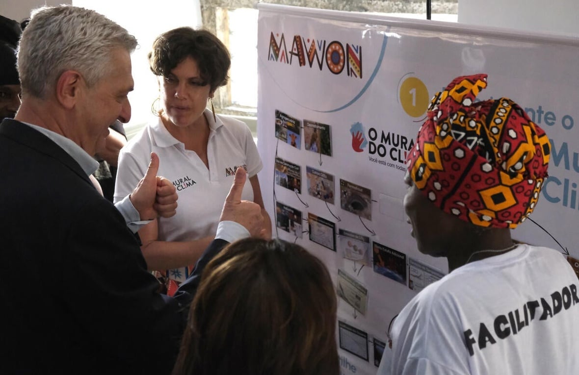 Two women and a man talk in front of an exhibition panel.