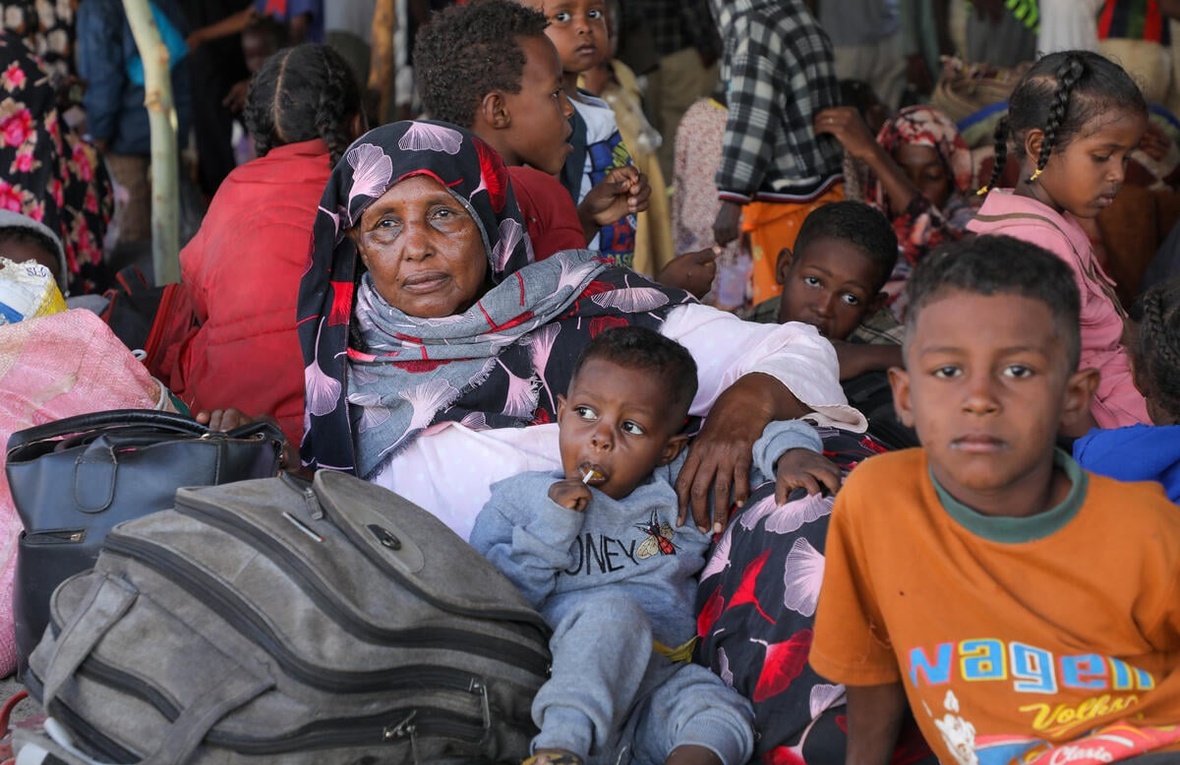 A woman sits on the floor surrounded by children and luggage