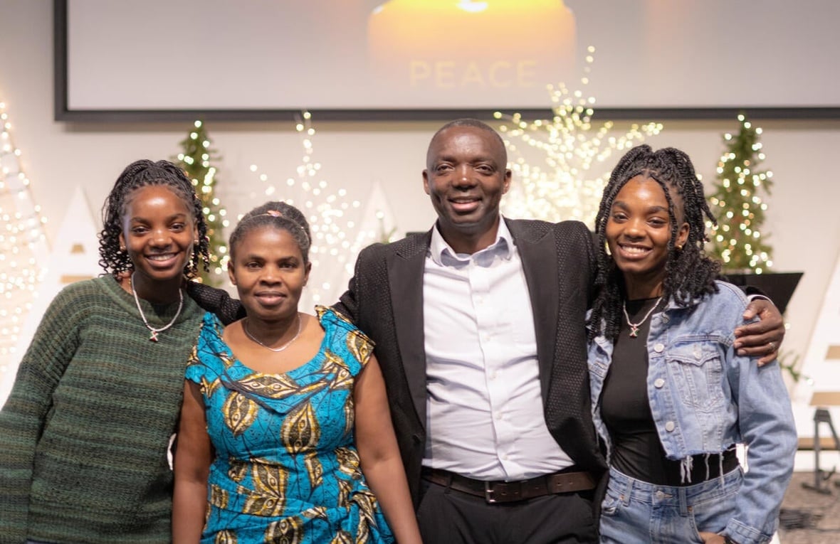 A pastor and his wife and two daughters pose for a photo in front of brightly coloured Chrismas tree.