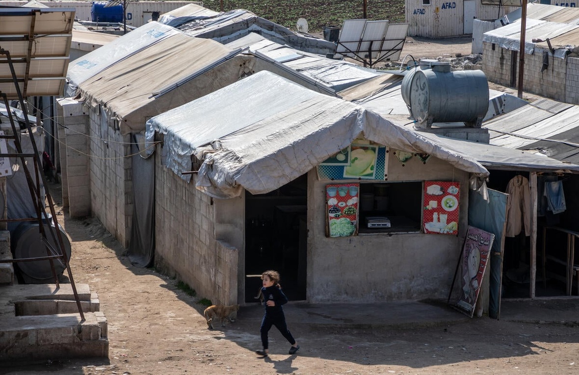 A young girl runs past breeze block shelters with tarpaulin covers in a displacement camp.