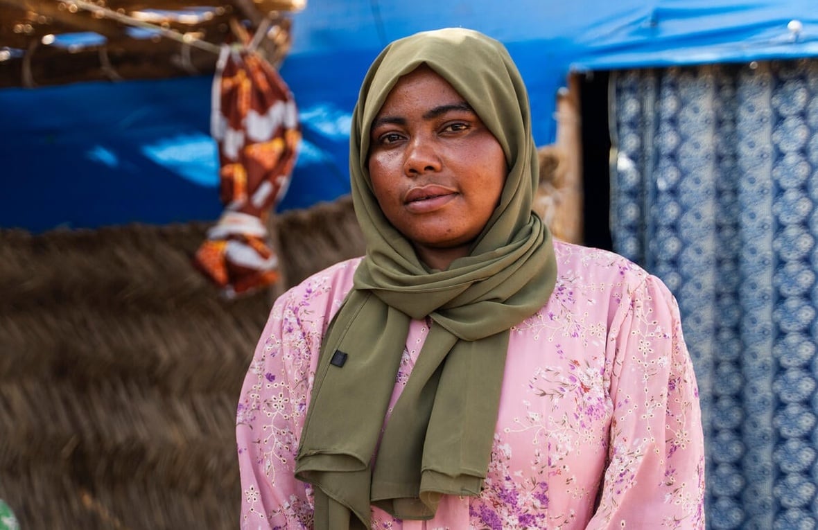 A portrait of a woman wearing a green headscarf standing in front of a shelter.