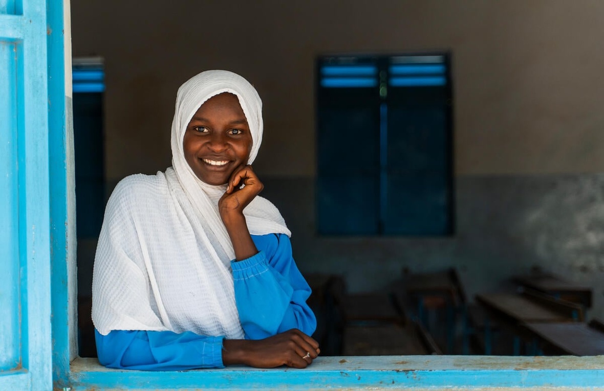 A young girl smiles at the camera, looking through an open window.