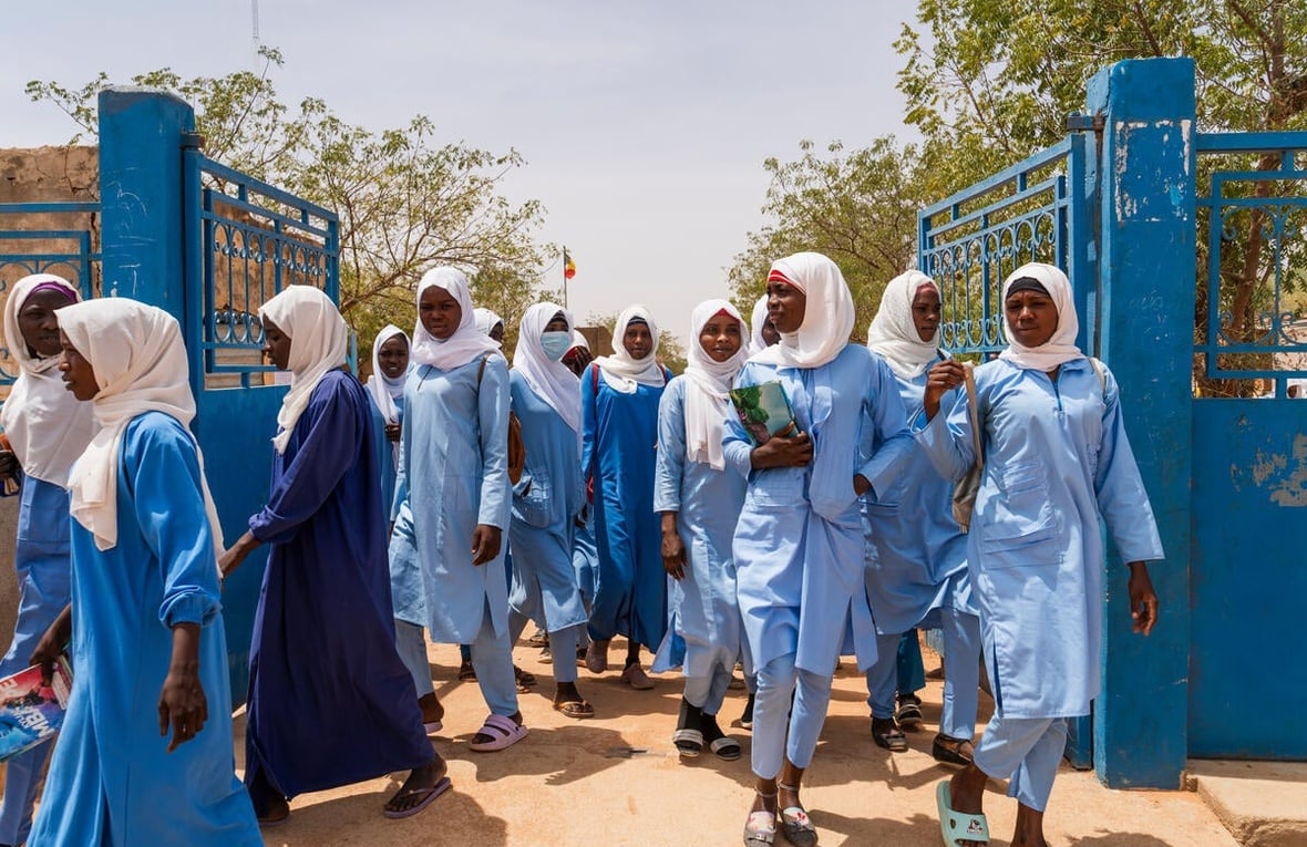 Female high school students carrying books and bags walk through school gates.