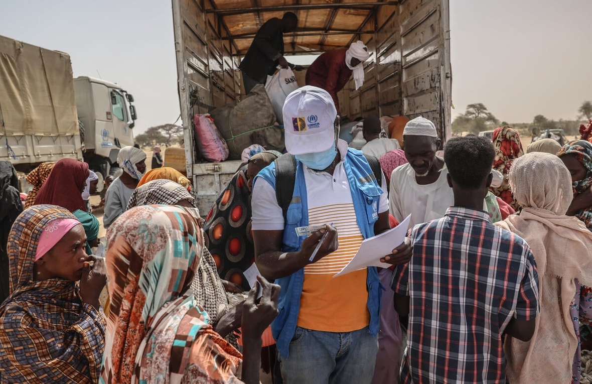 A UNHCR staff member checks documents in a group of people standing at the back of an open truck.