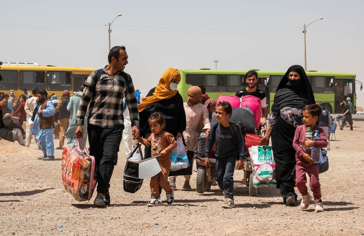 An Afghan family carries their belongings, walking away from two buses behind them.