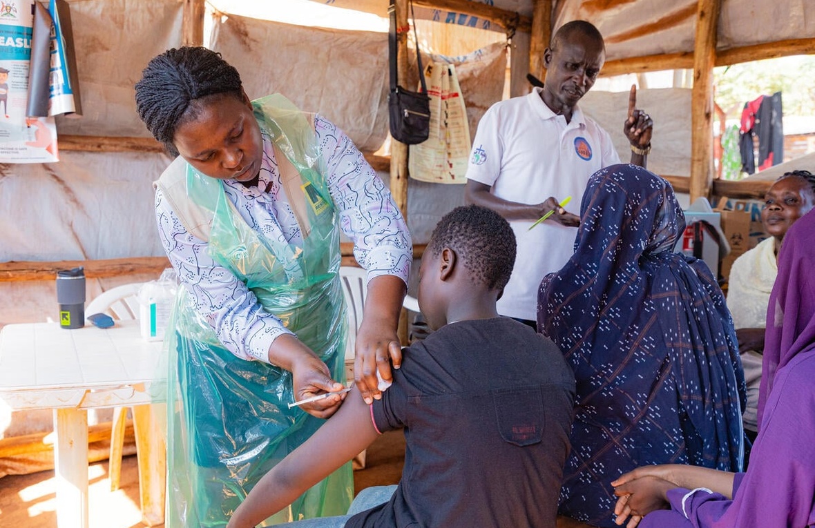 Several people receive vaccinations and other medical consultation in a makeshift shelter outdoors