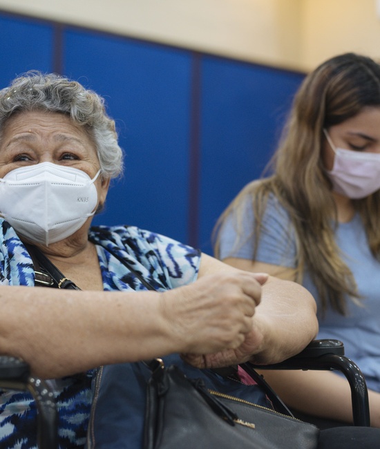 An old woman wearing a mask sits next to a young woman.