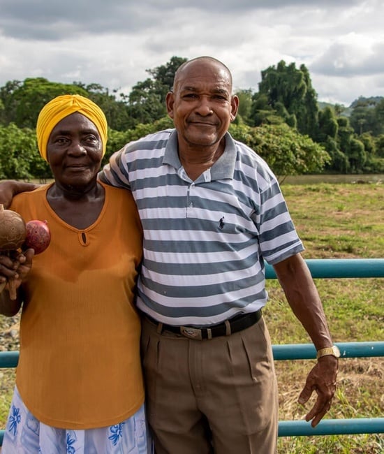 Elderly refugee couple stands in front of a field.