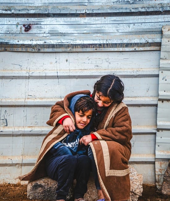 A young Syrian refugee wraps herself and her younger brother in a blanket as they sit outside in the cold in the Zaatari refugee camp.