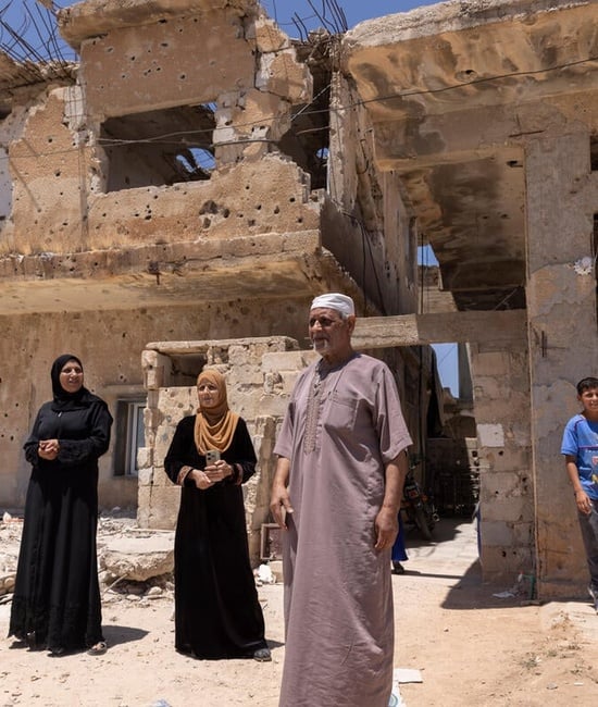 A family of four refugee returnees stand in front of a partially-collapsed building – their home in Daraa, southern Syria