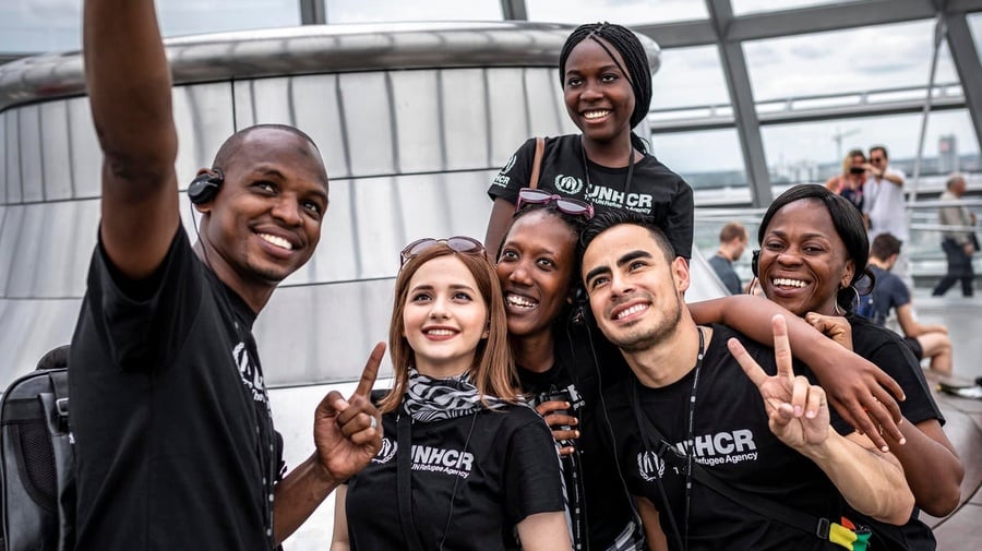 A group of young people in UNHCR t-shirts take a selfie. 