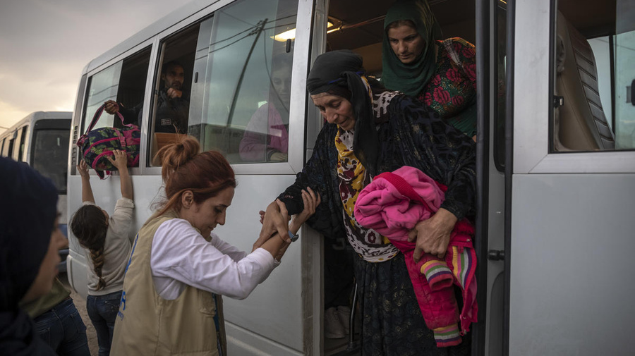 A UNHCR staff member helps an elderly Syrian refugee woman to step down from a bus. 
