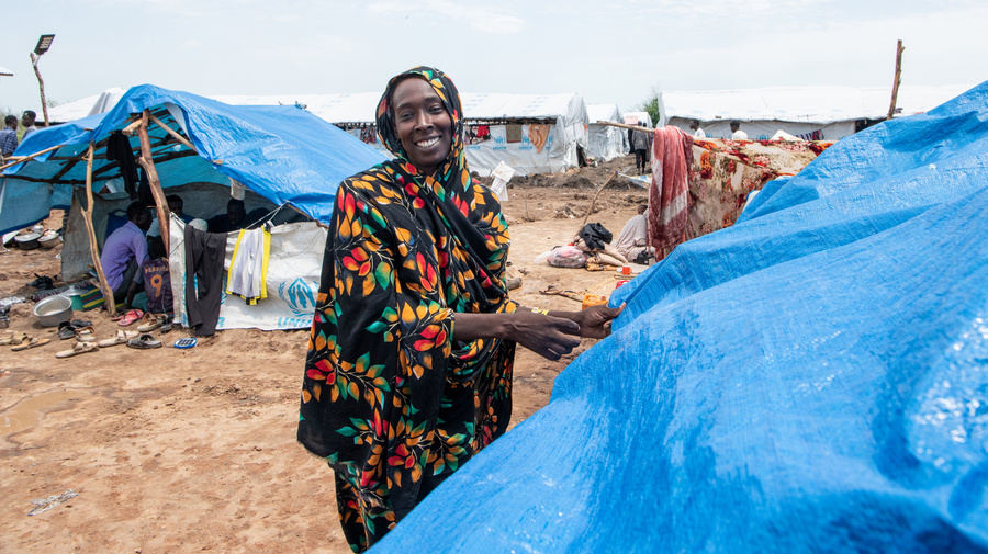 A woman smiles as she pulls a blue tarpaulin into place over a makeshift shelter.
