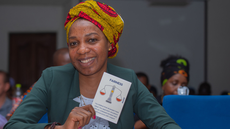 A smiling woman sits at a desk holding up a card that says 'Fairness, justice: You believe that all people have value. You approach situations with an unbiased mindset and treat everyone with respect.'