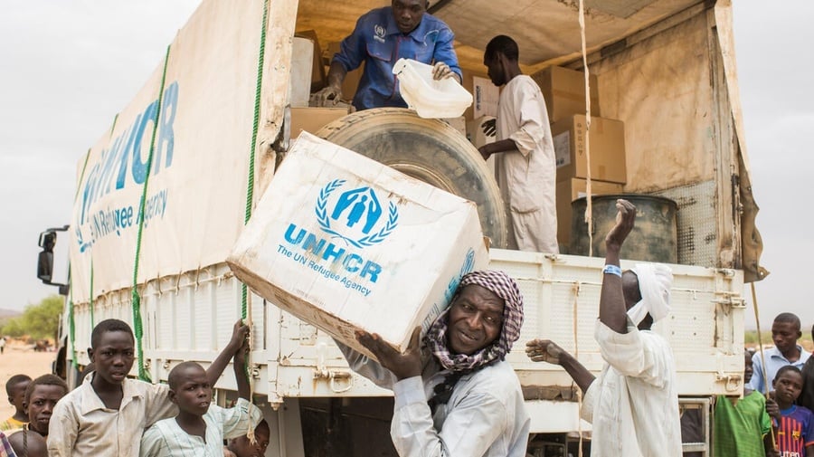 UNHCR staff unload boxes of emergency supplies from a truck in a refugee camp. 