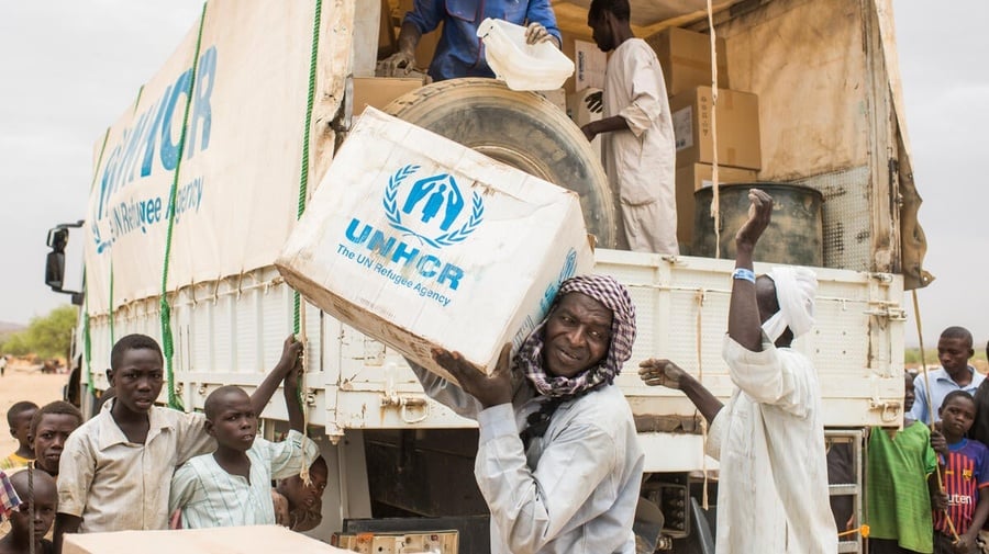 UNHCR staff unload boxes of emergency supplies from a truck in a refugee camp. 