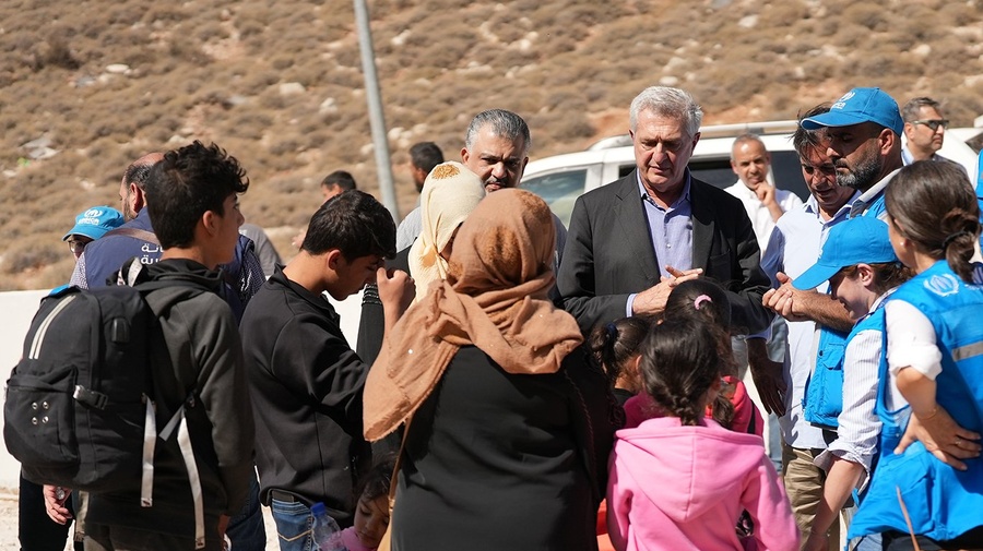 A man in a suit and others in UN clothing talk to a family outside with a vehicle in the background