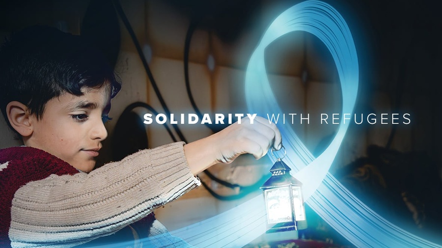 A young boy is holding a small lantern in a dark room. A blue, shiny and flying ribbon floats around the lantern. The text reads "solidarity with refugees".