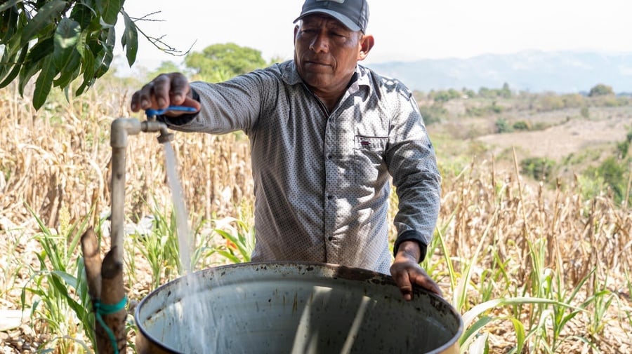 Salvadoran farmer José fills a metal drum with water on his farm.