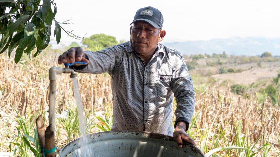 Salvadoran farmer José fills a metal drum with water on his farm.