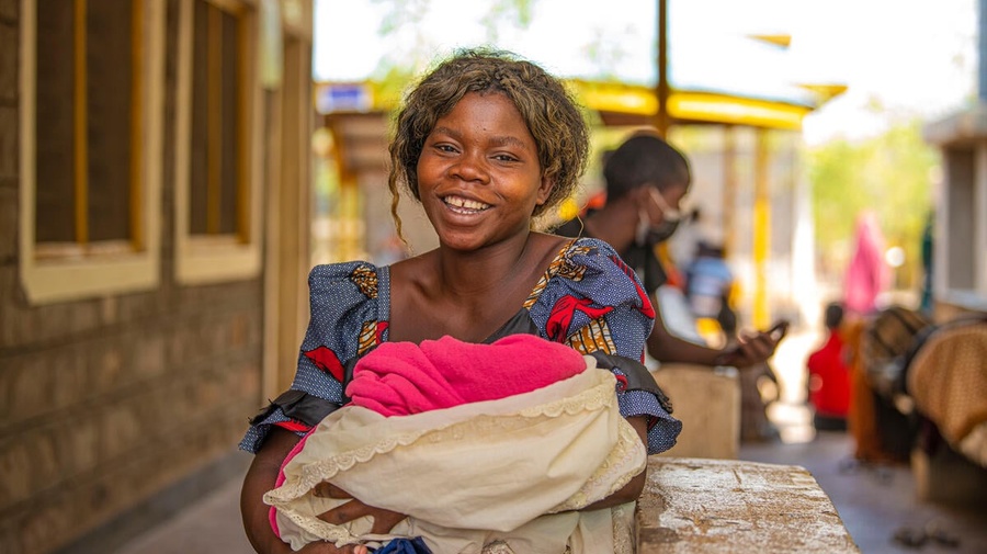 A smiling woman carries a bundle in her arms