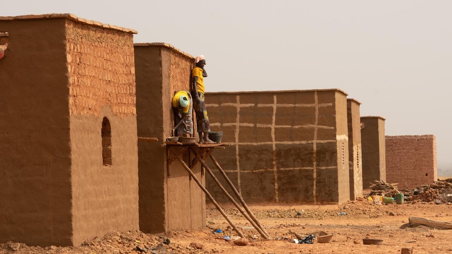 Two people apply mud stucco to the walls of a house under construction in Burkina Faso.