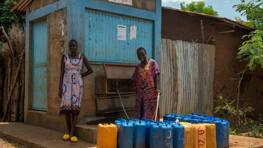 Two women fill jerry cans with water from an outdoor tap. 