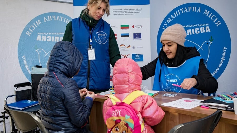 A psychologist supports a parent and child at a desk, with a UNHCR Ukraine banner behind them