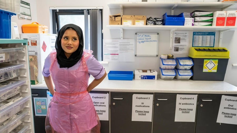 A hospital worker inside a medicine storage room, surrounded by shelves of supplies.
