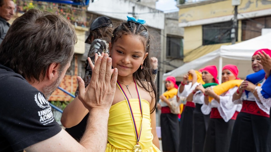 A UNHCR representative high-fives a young girl in a yellow dress