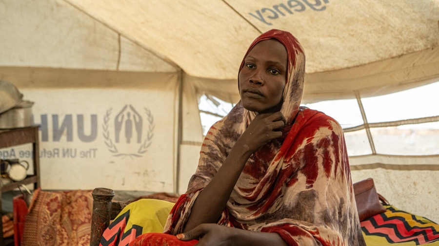 A woman sits on a yellow bed inside a UNHCR tent.