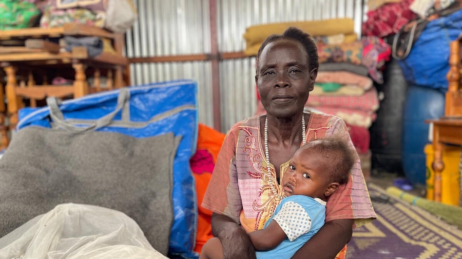 A woman sits on a carpet in an aid distribution center, with a baby on her lap.
